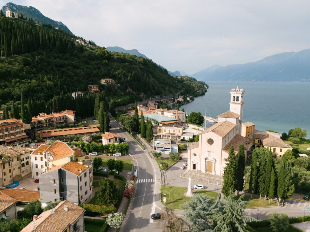 Luftaufnahme eines Dorfes am See in Italien mit einer Kirche, rot gedeckten Gebäuden und grünen Hügeln - ein zauberhafter Ort für eine von einem erfahrenen Hochzeitsplaner geplante Destination Wedding.