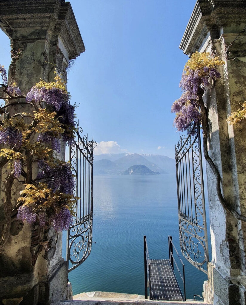 Schmiedeeiserne Tore geben den Blick frei auf den Comer See mit seinen violetten Glyzinien und den fernen Bergen - eine Traumkulisse in Italien, perfekt für jeden Hochzeitsplaner.
