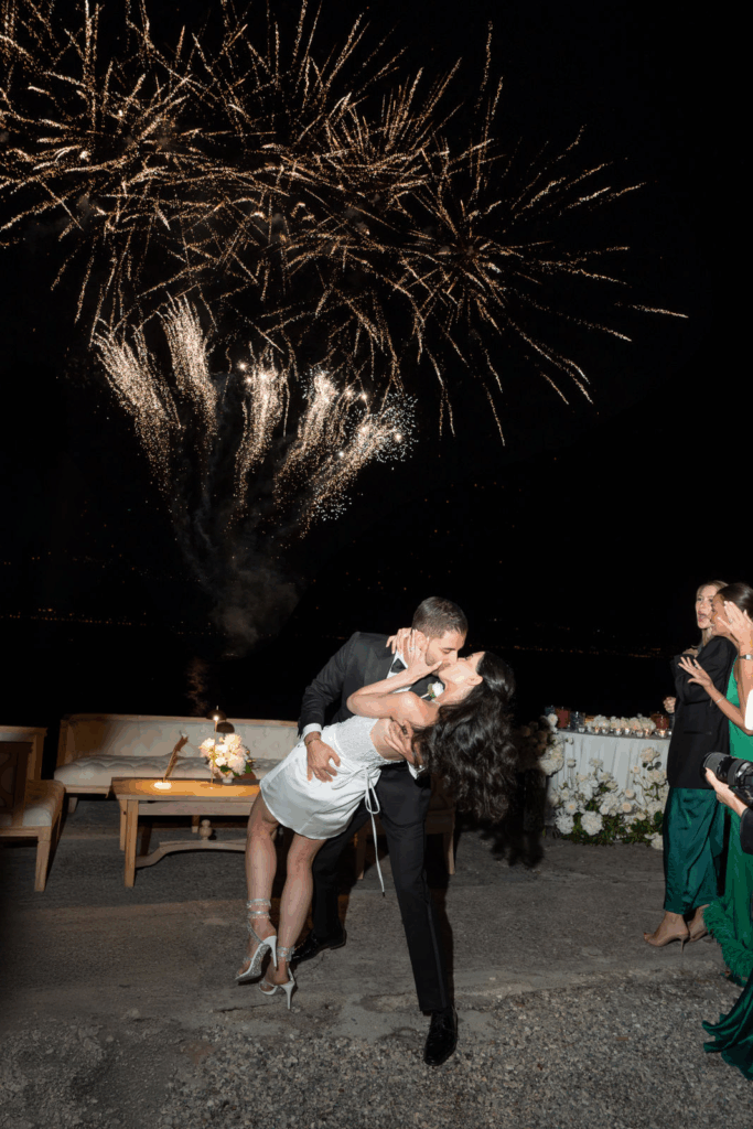 Ein Paar küsst und tanzt unter einem nächtlichen Feuerwerk am Comer See, umgeben von formell gekleideten Gästen - ein unvergesslicher Moment, der von einem erfahrenen Hochzeitsplaner geschaffen wurde.